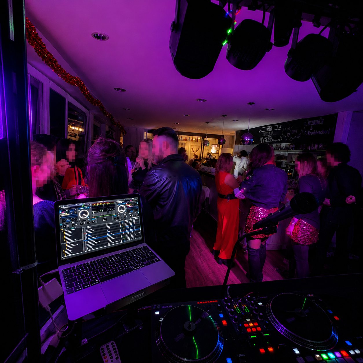 Tanzende Gäste im Clublicht hinter dem DJ-Setup